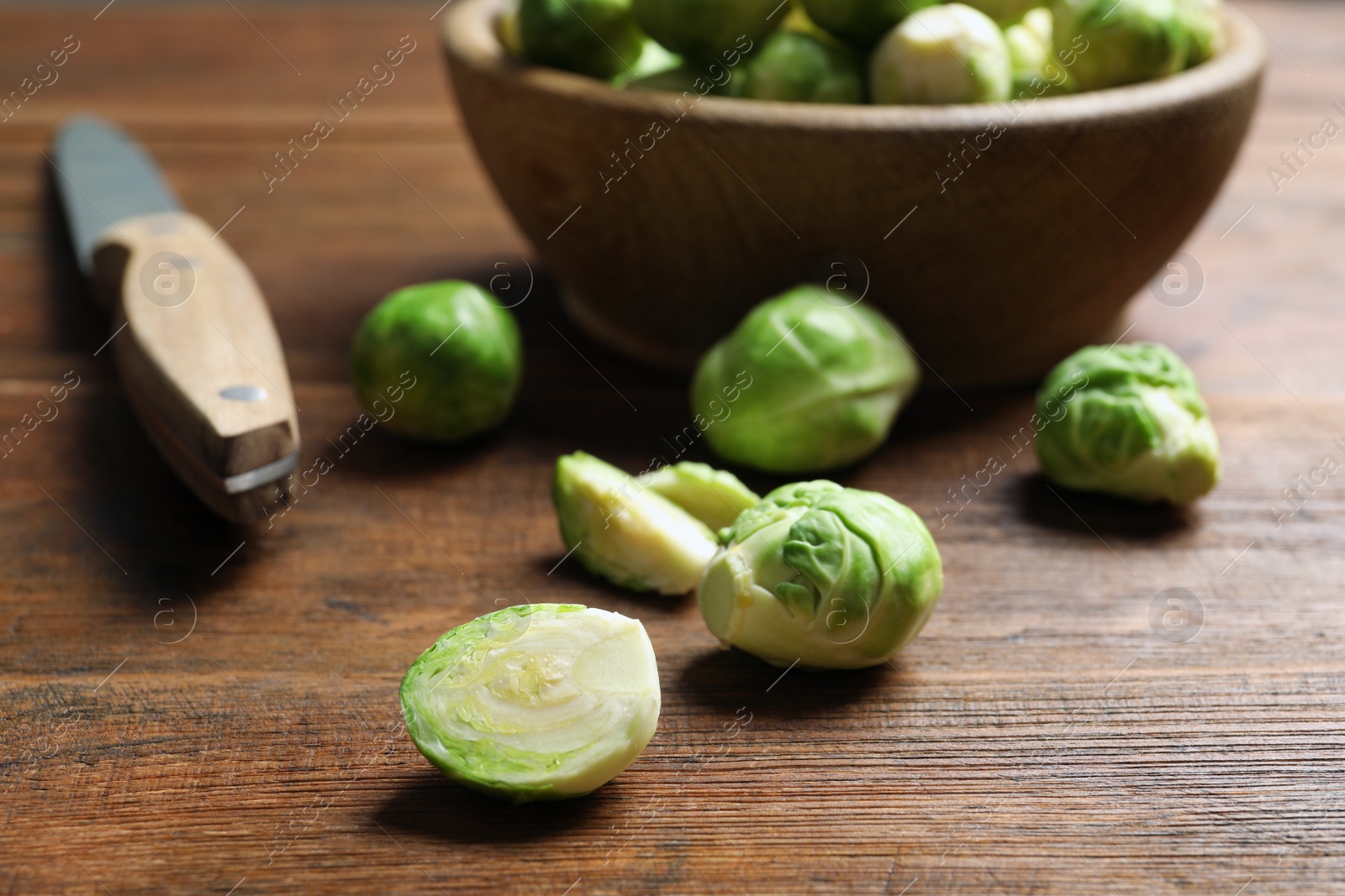 Photo of Fresh Brussels sprouts, bowl and knife on table, closeup