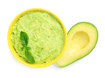 Bowl of tasty guacamole with basil and cut avocado on white background, top view