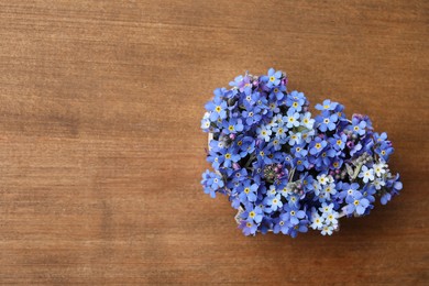Heart of beautiful blue forget-me-not flowers on wooden table, top view. Space for text