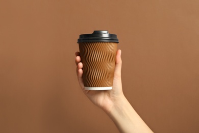 Photo of Woman holding takeaway paper coffee cup on brown background, closeup