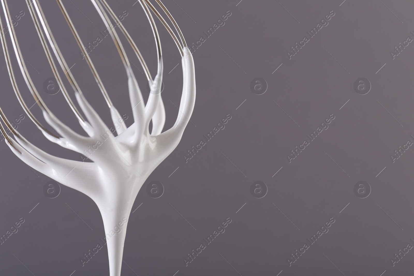 Photo of Whisk with whipped cream on grey background, closeup. Space for text