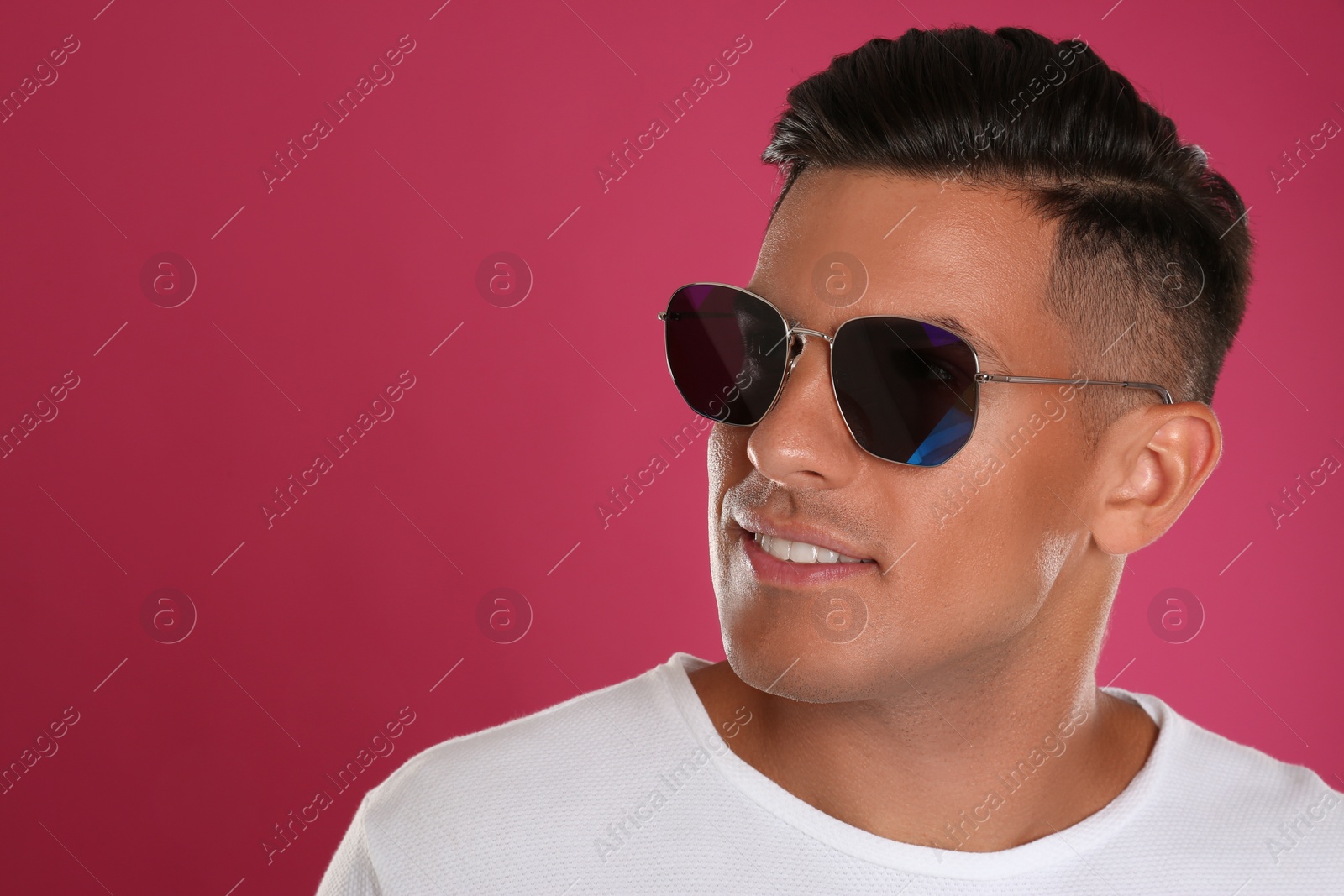 Photo of Handsome man wearing sunglasses on pink background, closeup. Space for text