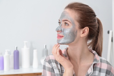 Young woman with cleansing mask on her face in bathroom, space for text. Skin care