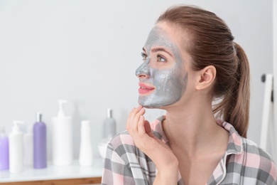 Photo of Young woman with cleansing mask on her face in bathroom, space for text. Skin care