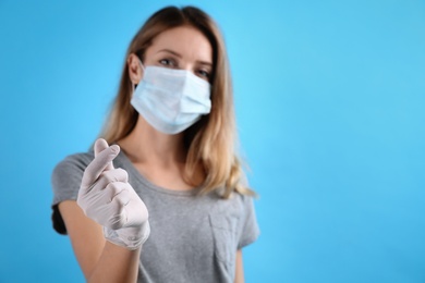 Young woman in medical gloves and protective mask showing heart gesture against light blue background, focus on hand. Space for text
