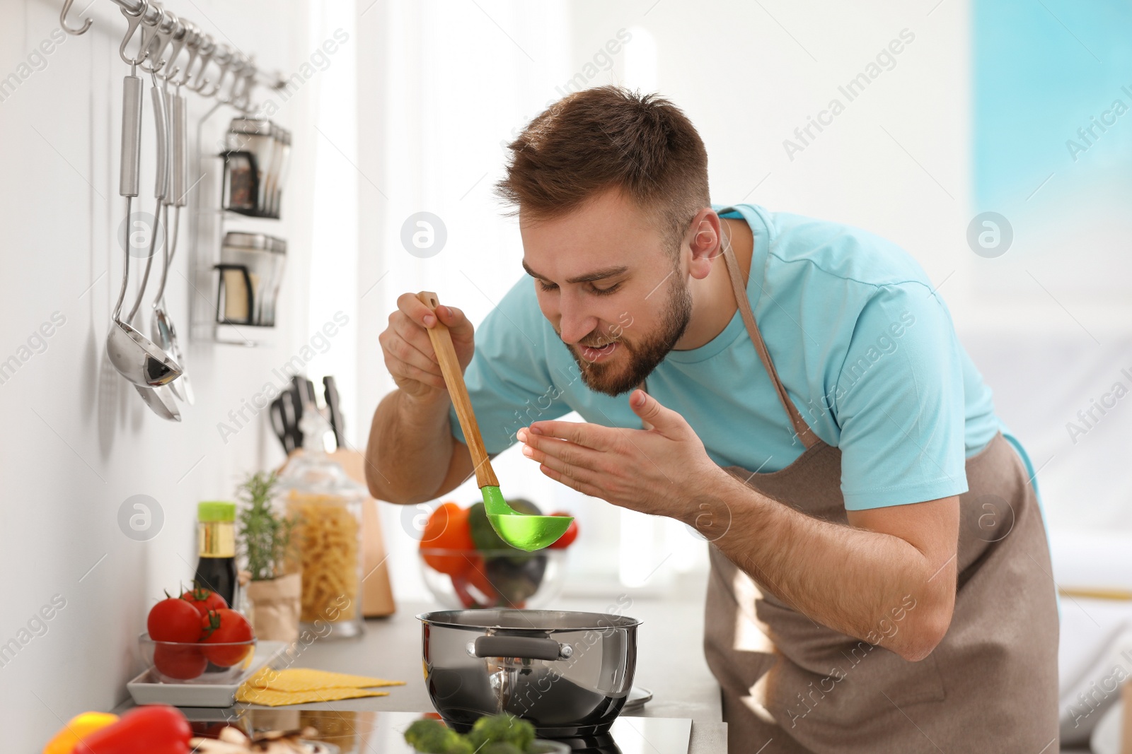 Photo of Young man cooking delicious soup in kitchen