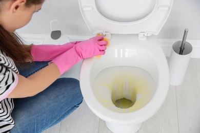 Photo of Woman cleaning toilet bowl in bathroom, closeup