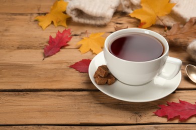 Cup of hot tea and autumn leaves on wooden table, space for text