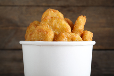 Bucket with tasty chicken nuggets on wooden background, closeup