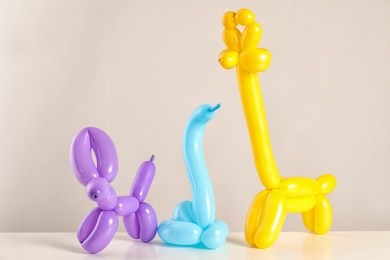 Animal figures made of modelling balloons on table against color background