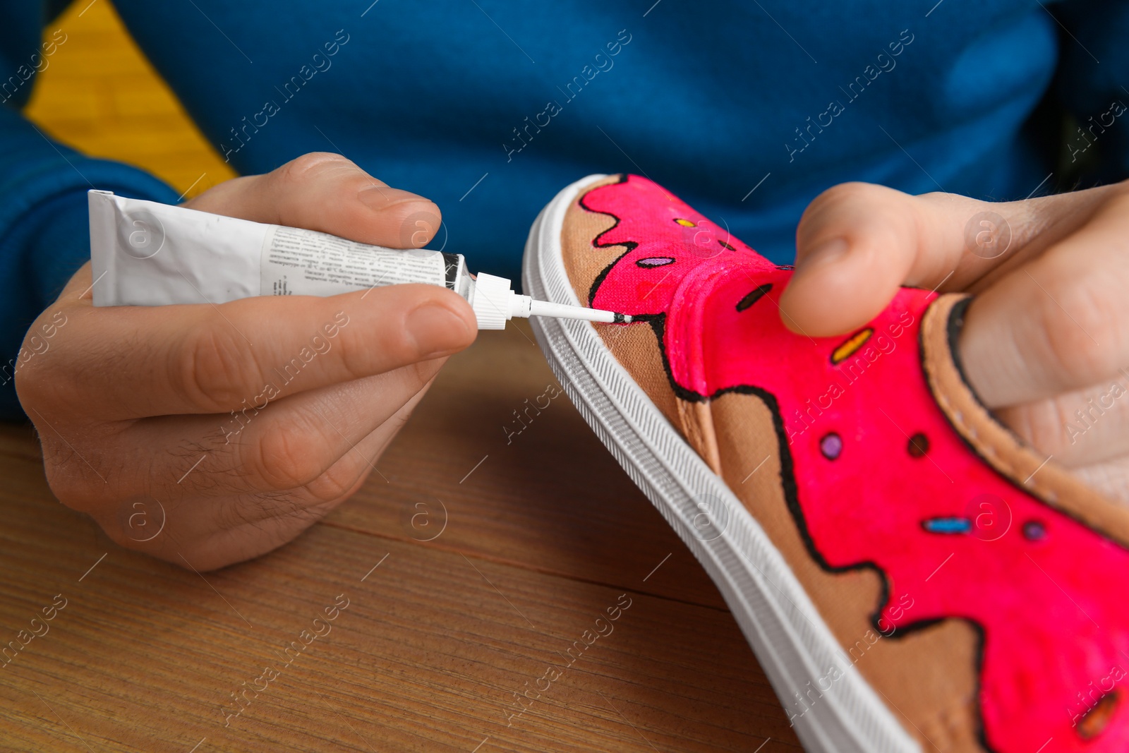 Photo of Man painting on sneaker at wooden table, closeup. Customized shoes