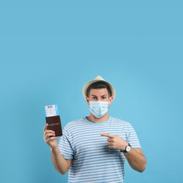 Male tourist in protective mask holding passport with ticket on turquoise background