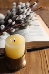 Photo of Burning candle, Bible and willow branches on wooden table, closeup