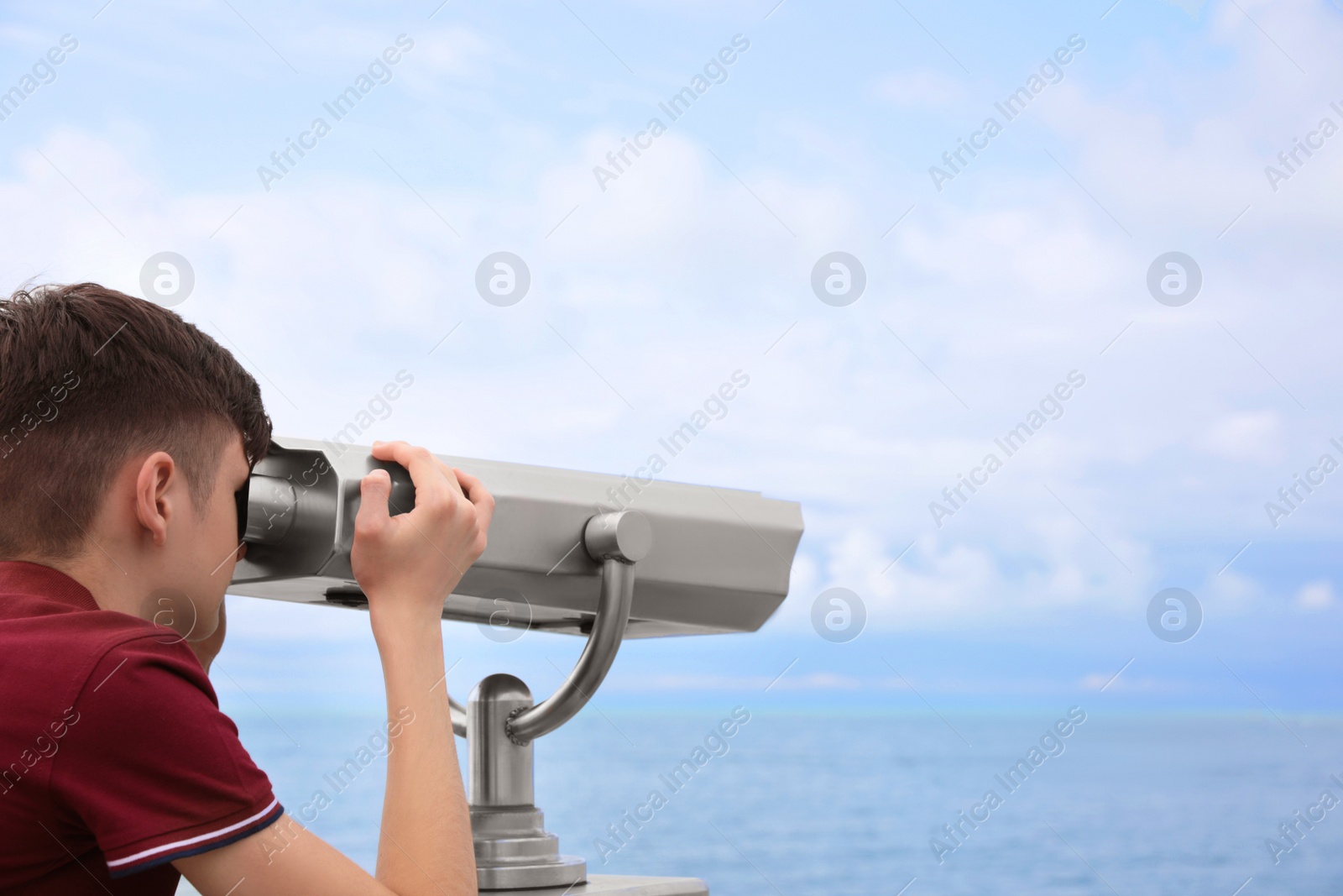 Photo of Teenage boy looking through mounted binoculars at mountains. Space for text