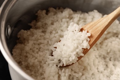 Photo of Pot with delicious rice and wooden spoon, closeup