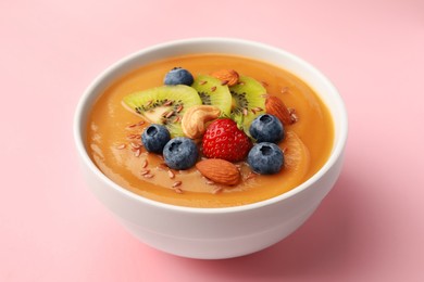 Photo of Delicious smoothie bowl with fresh berries, kiwi and nuts on pale pink background
