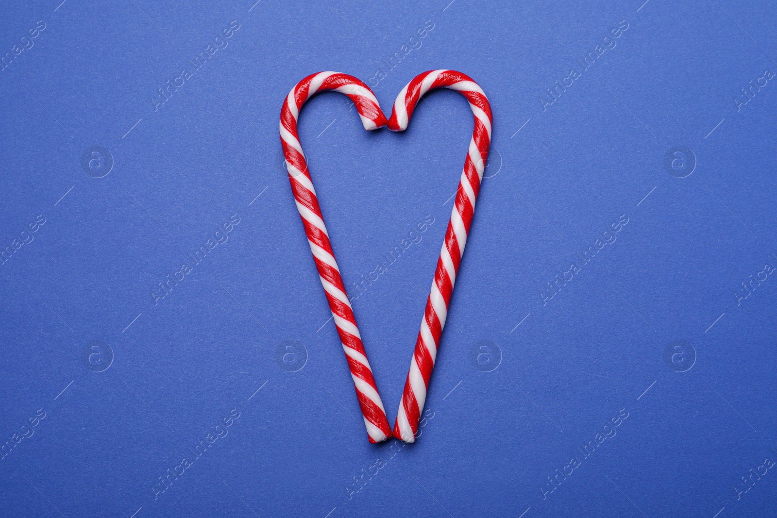 Photo of Heart shape made of sweet Christmas candy canes on blue background, top view