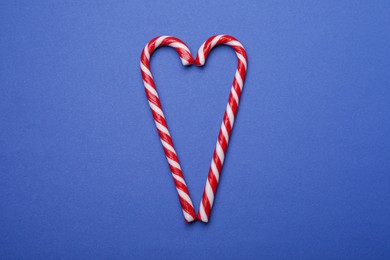 Photo of Heart shape made of sweet Christmas candy canes on blue background, top view