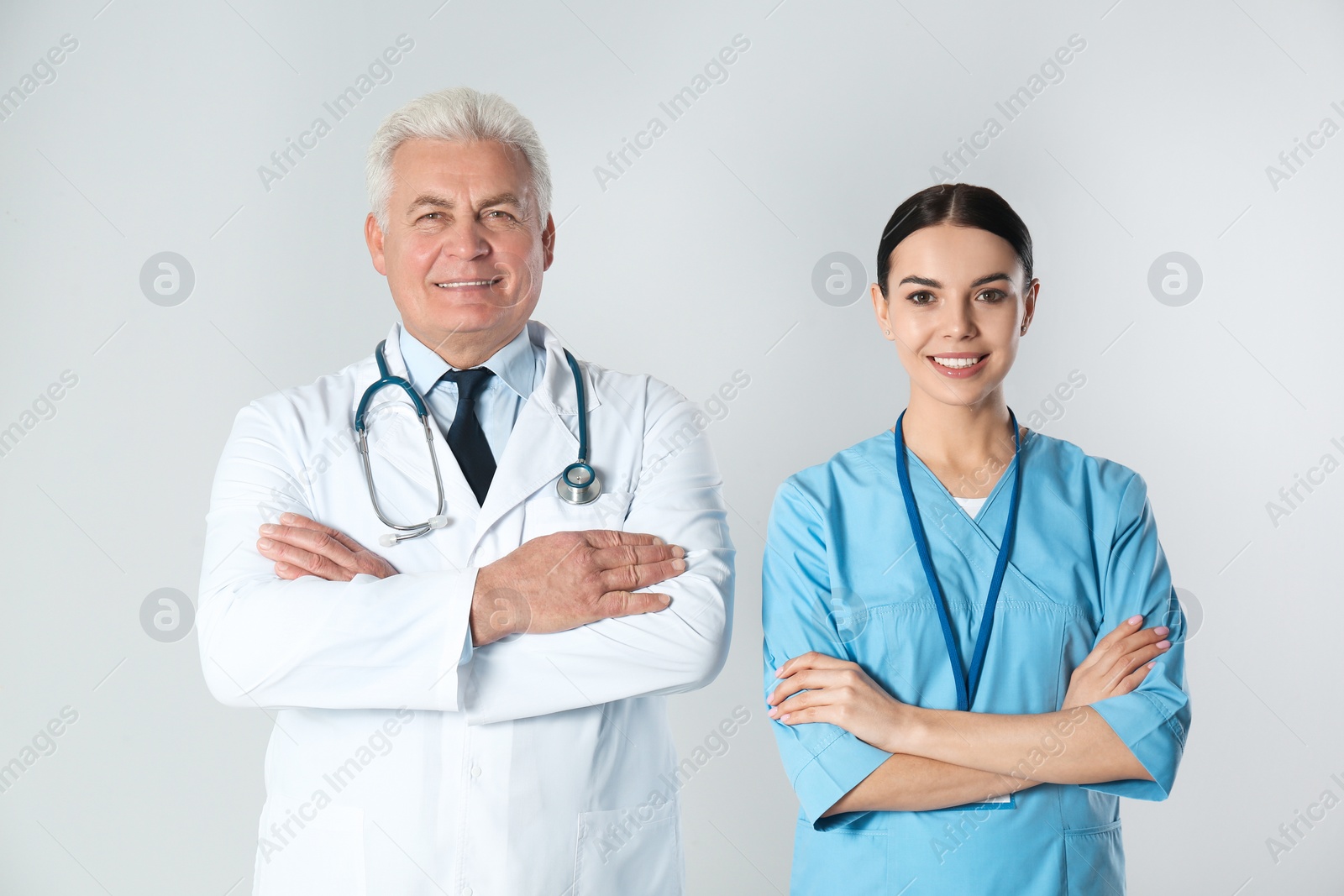 Photo of Senior doctor and young nurse against light background