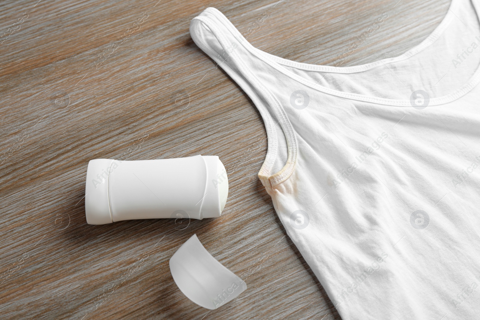 Photo of White undershirt with stain and deodorant on wooden background