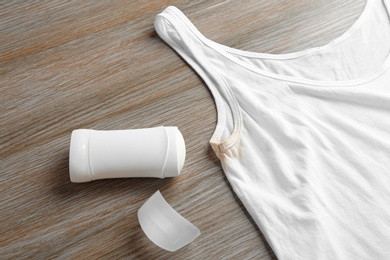 Photo of White undershirt with stain and deodorant on wooden background