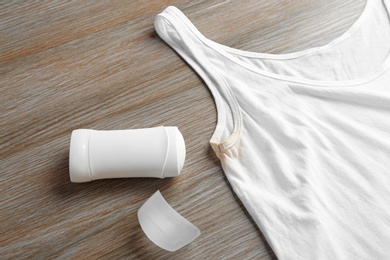 White undershirt with stain and deodorant on wooden background