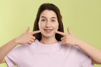 Portrait of smiling woman pointing at her dental braces on light green background