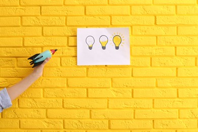 Photo of Woman holding toy rocket near yellow brick wall with lamps drawing, closeup. Startup concept
