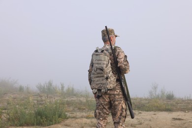 Photo of Man wearing camouflage with hunting rifle and backpack outdoors, back view