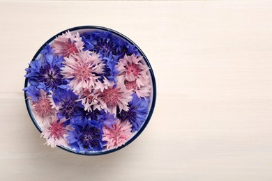 Beautiful colorful cornflowers in bowl on white wooden table, top view. Space for text