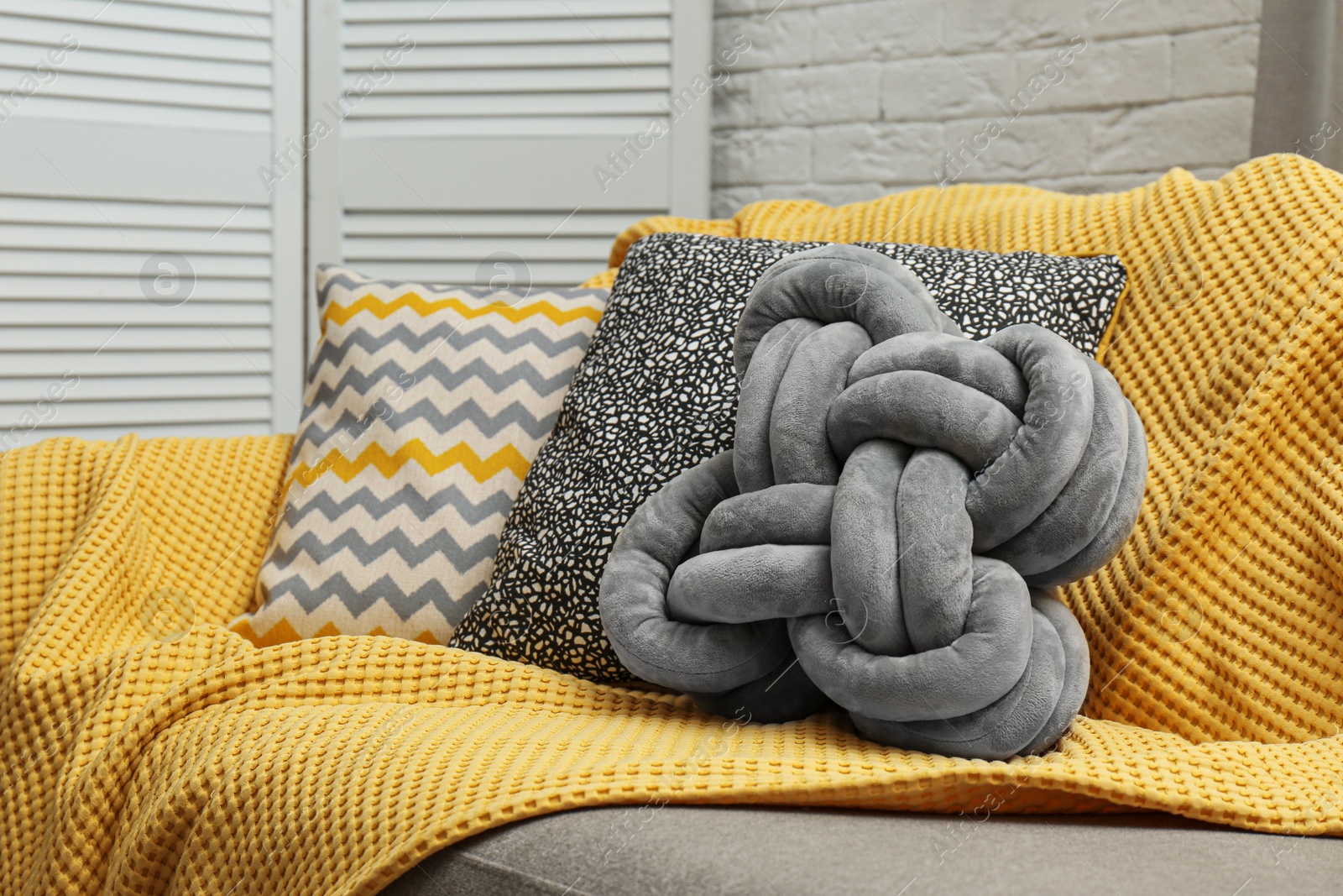 Photo of Soft pillows and yellow plaid on sofa in living room