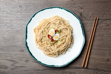 Plate of tasty noodles and chopsticks served on wooden table, flat lay