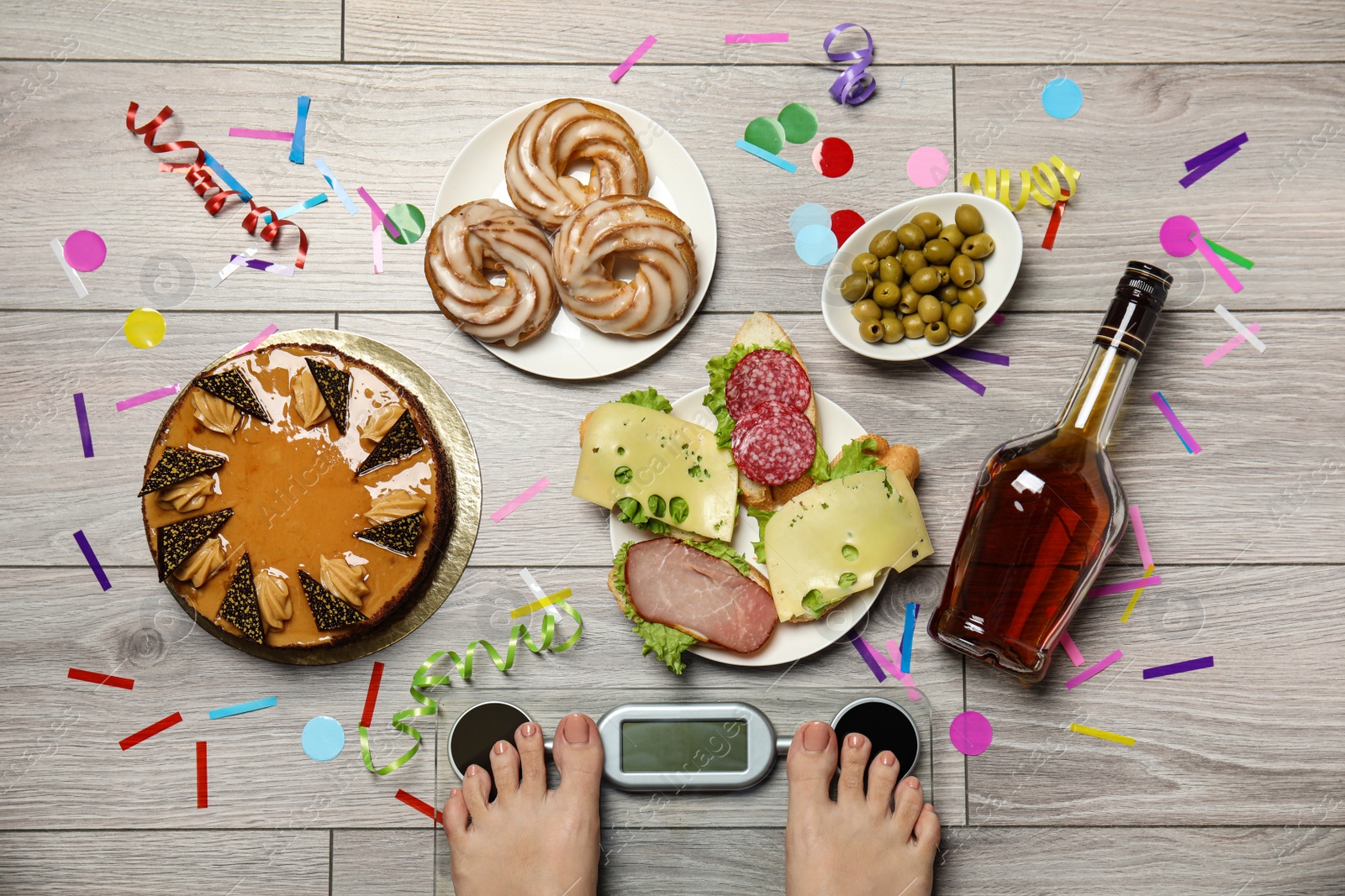 Photo of Woman using scale surrounded by food and alcohol after party on floor, top view. Overweight problem