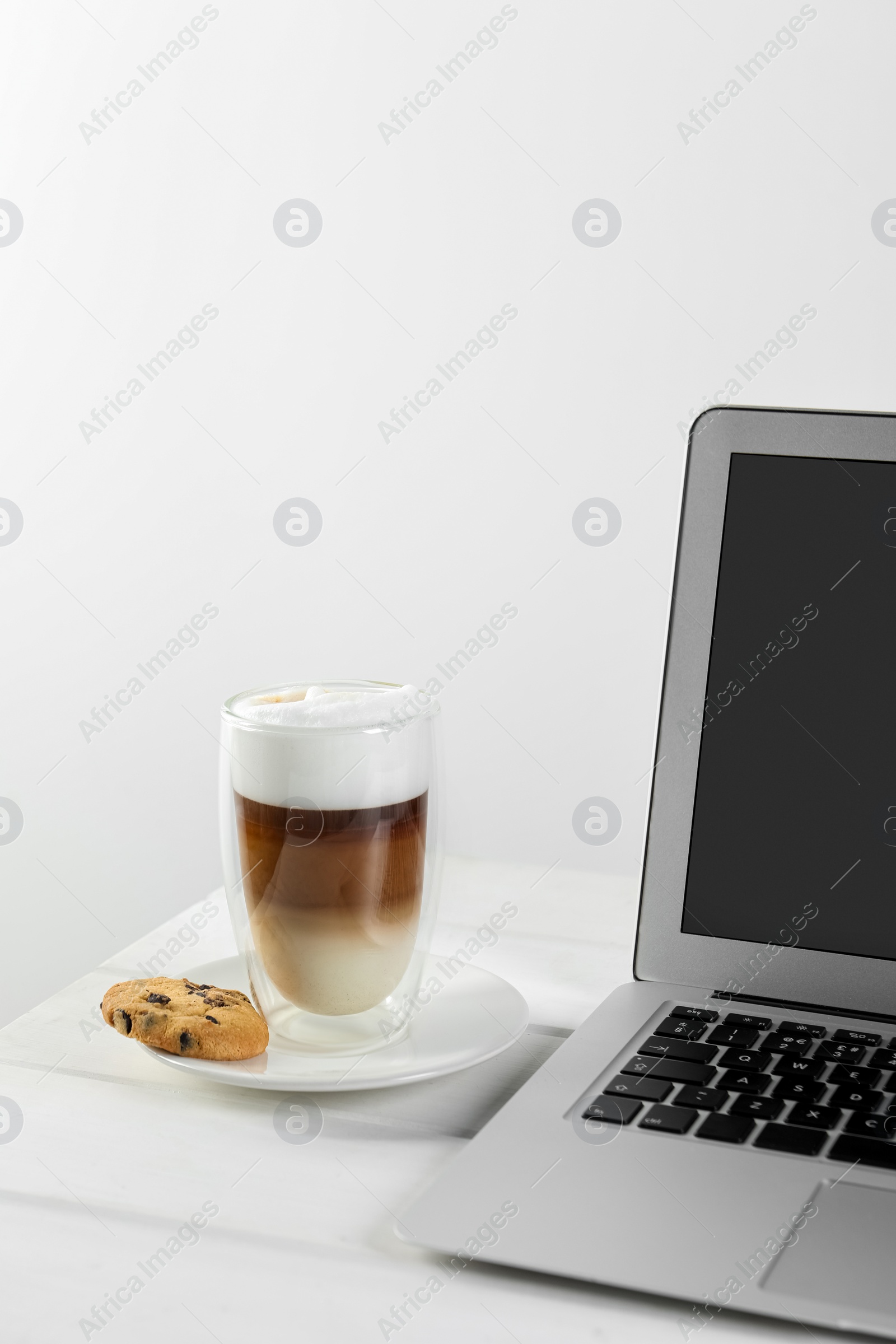 Photo of Chocolate chip cookie, latte and laptop on white wooden table indoors