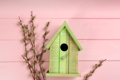 Photo of Beautiful green bird house and willow branches on pink wooden background. Spring flat lay composition