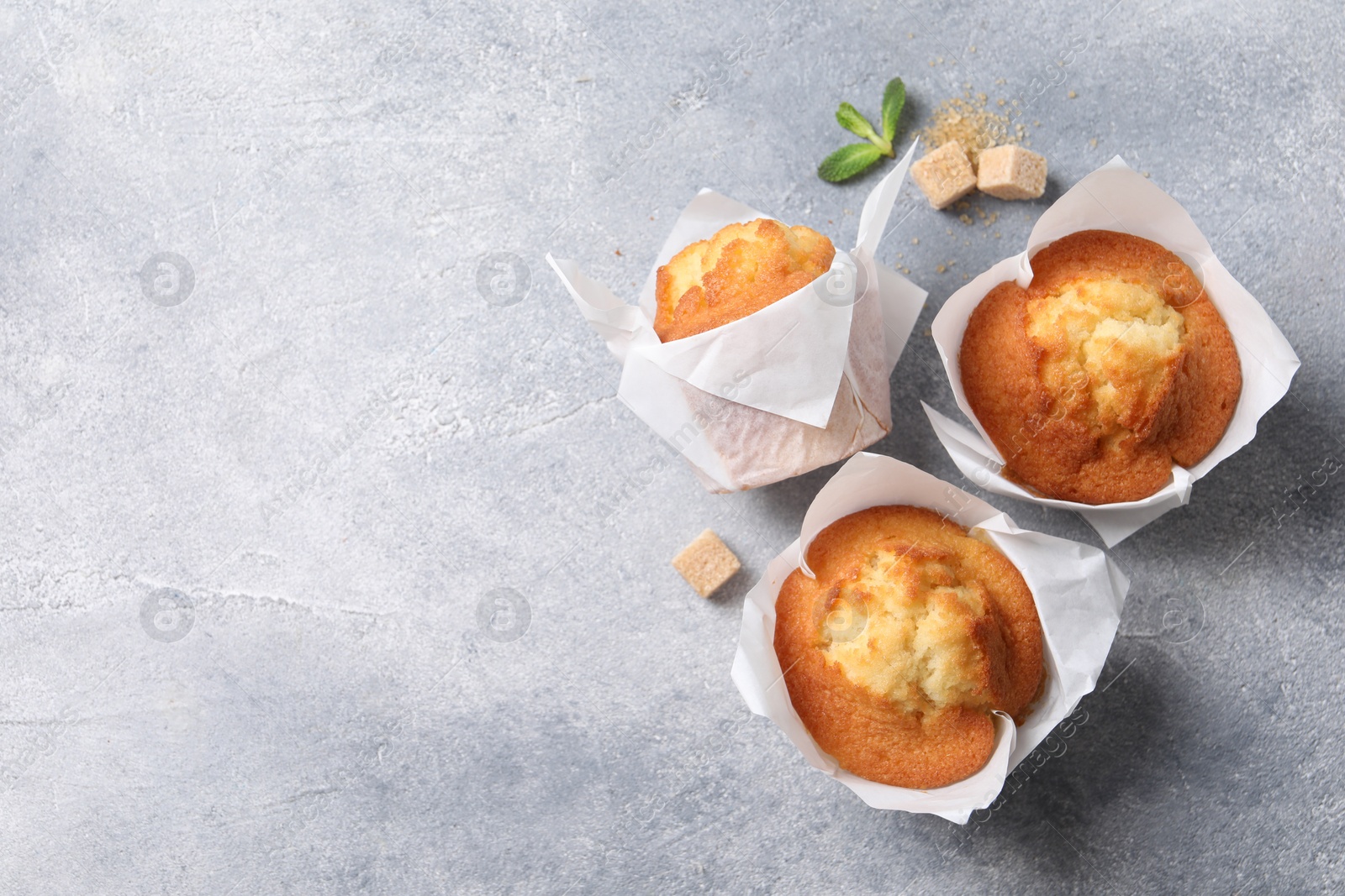 Photo of Delicious sweet muffins and brown sugar on light grey textured table, flat lay. Space for text