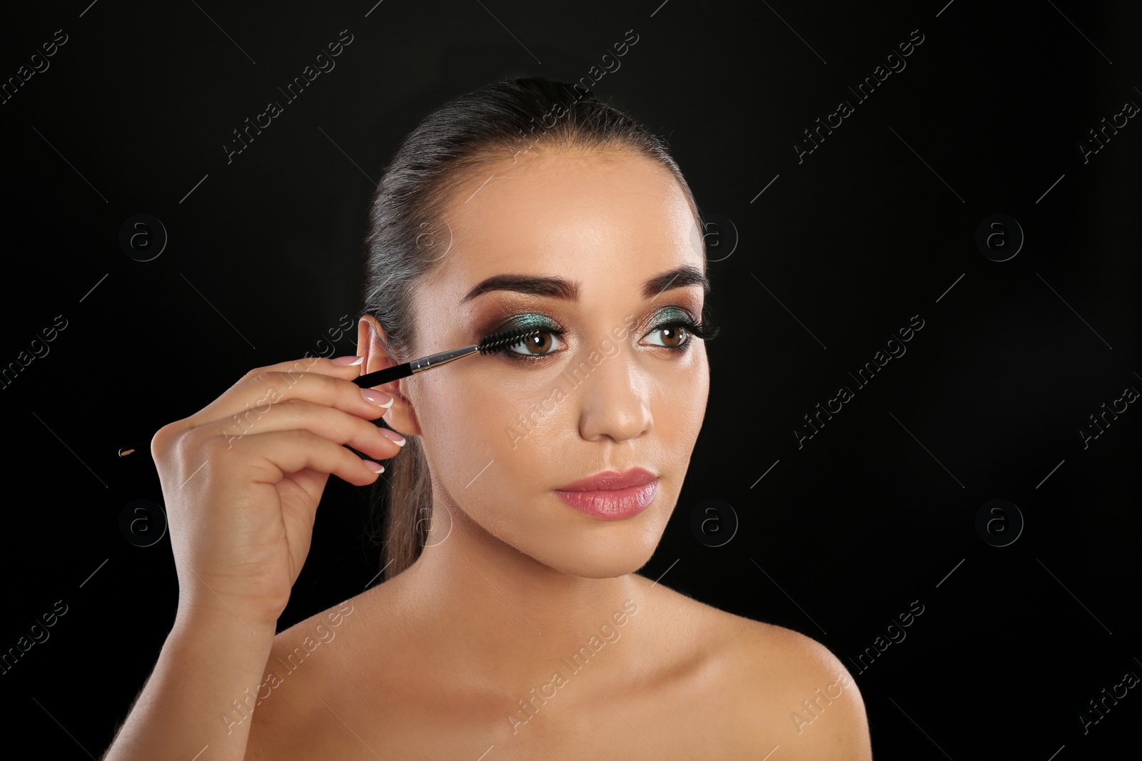 Photo of Portrait of young woman brushing eyelash extensions on black background
