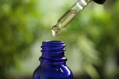 Pipette and bottle of essential oil on blurred background, closeup