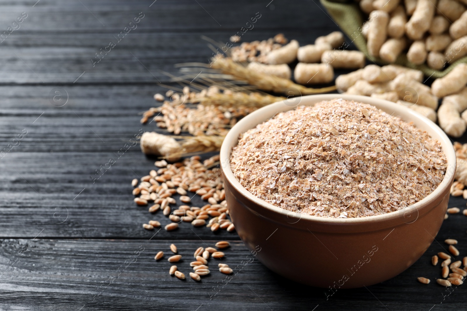 Photo of Bowl of wheat bran on black wooden table, space for text