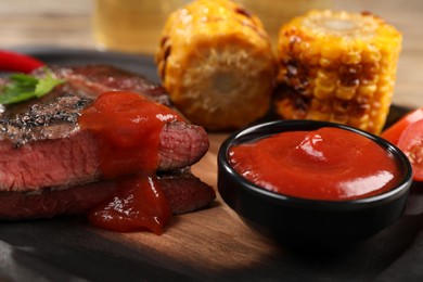 Photo of Delicious fried steak with sauce and grilled corn on wooden table, closeup