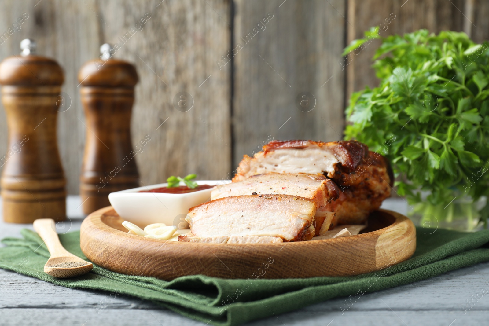 Photo of Pieces of baked pork belly served with sauce on grey wooden table