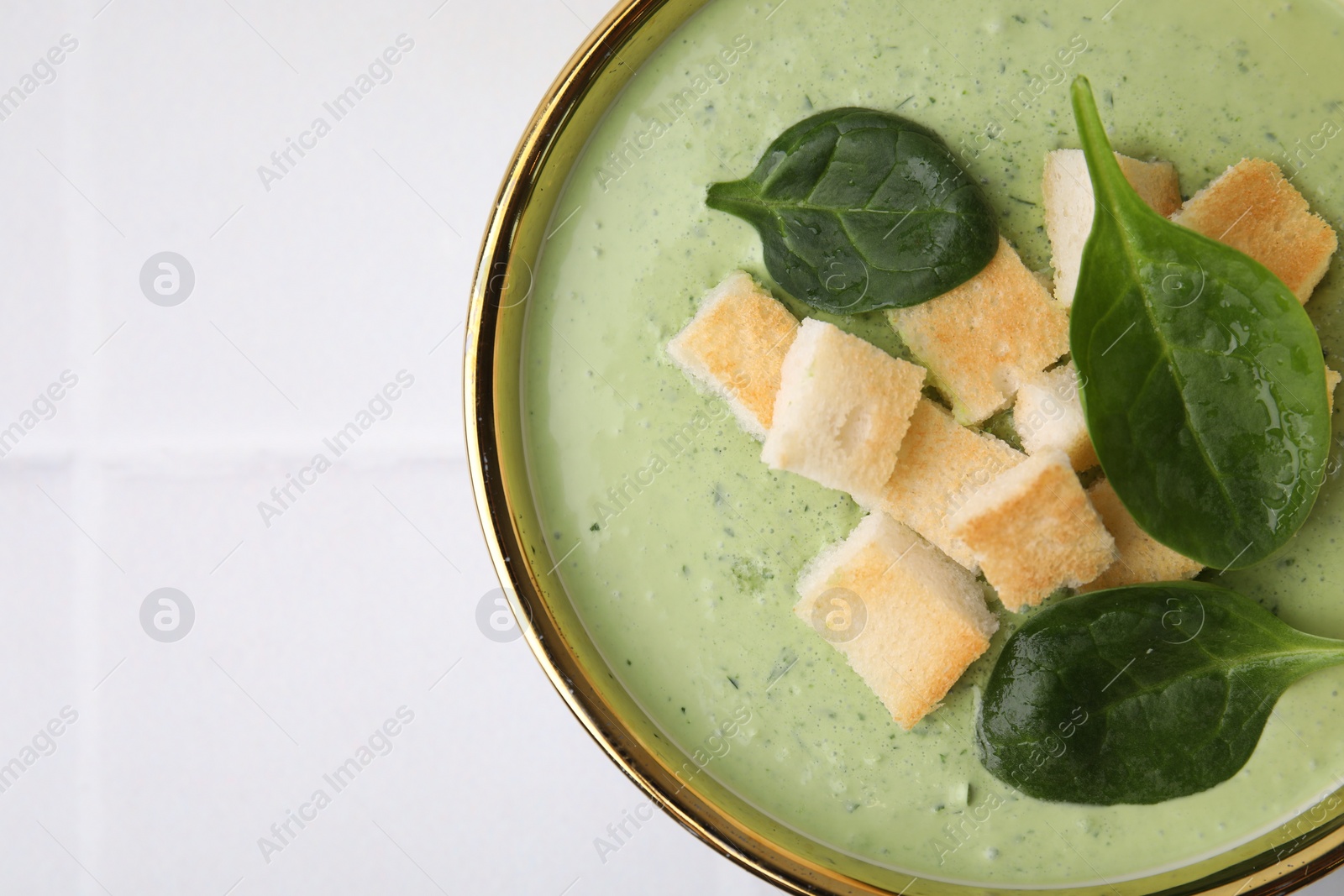 Photo of Delicious spinach cream soup with croutons in bowl on white tiled table, top view. Space for text