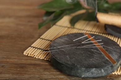 Photo of Grey stone coaster with acupuncture needles on wooden table. Space for text