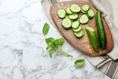 Photo of Fresh ripe cucumbers and basil on white marble table, flat lay. Space for text