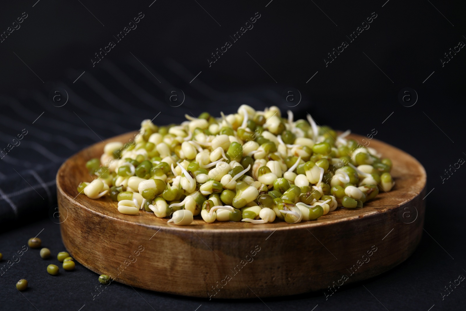 Photo of Wooden plate with sprouted green mung beans on black background, closeup