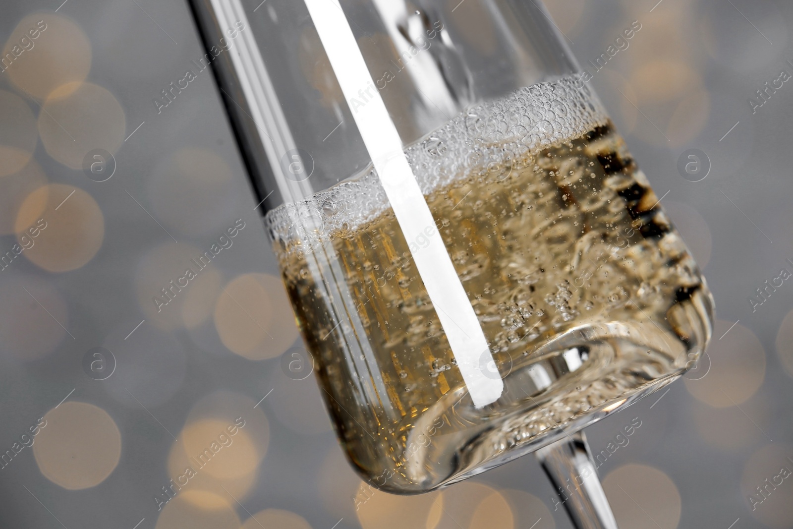 Photo of Pouring champagne into glass against blurred lights, closeup