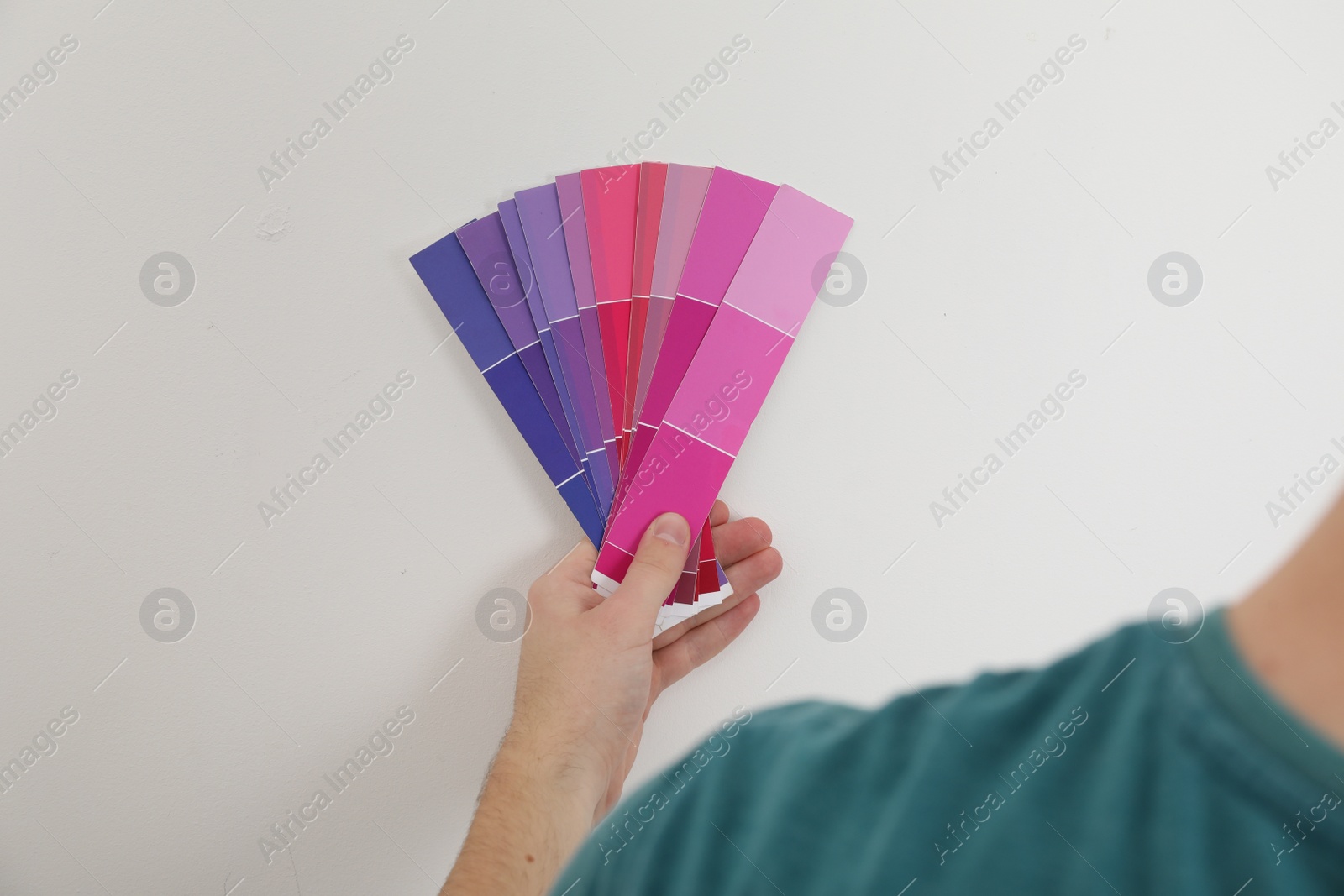 Photo of Man with palette choosing color for painting wall indoors, closeup. Interior design