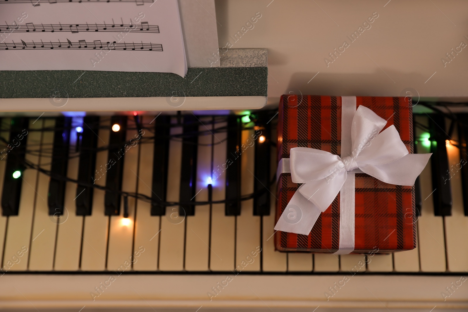 Photo of Gift box and fairy lights on piano keys, top view. Christmas music