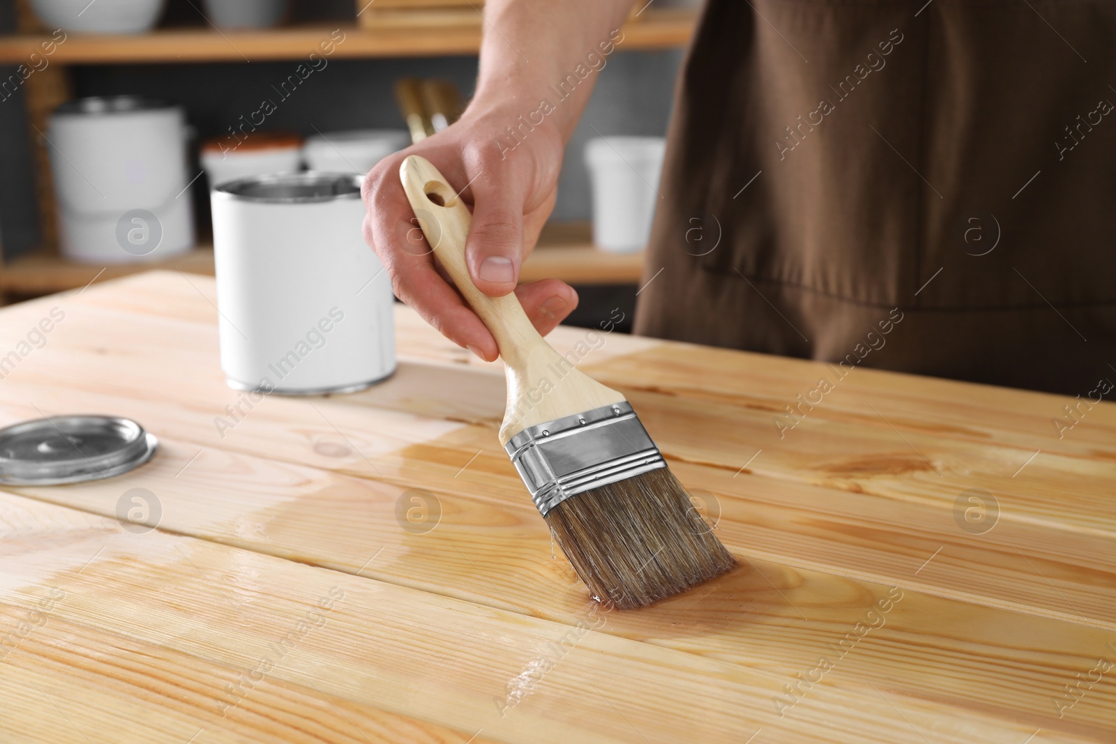 Photo of Man varnishing wooden surface with brush indoors, closeup