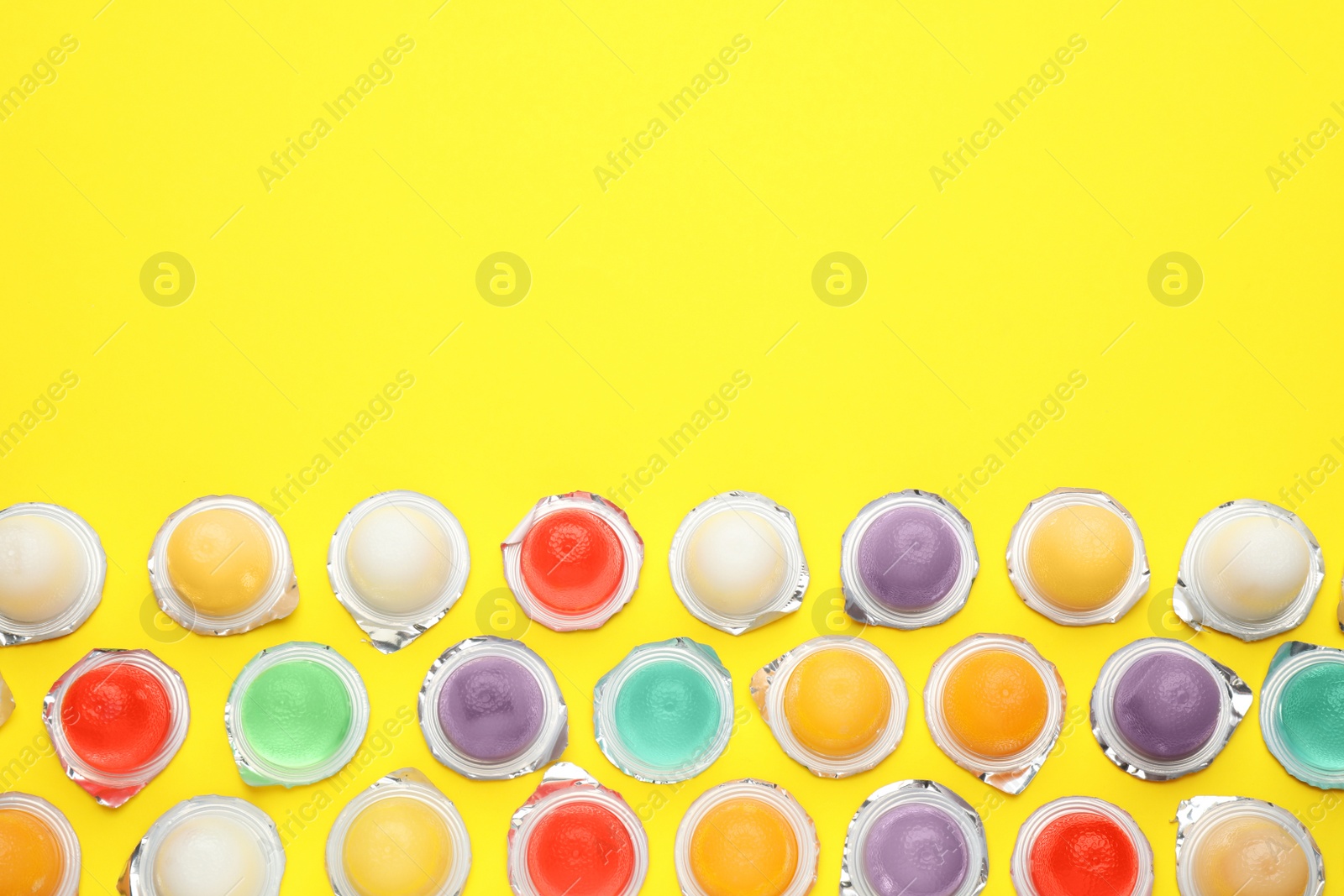 Photo of Tasty bright jelly cups  on yellow background, flat lay. Space for text